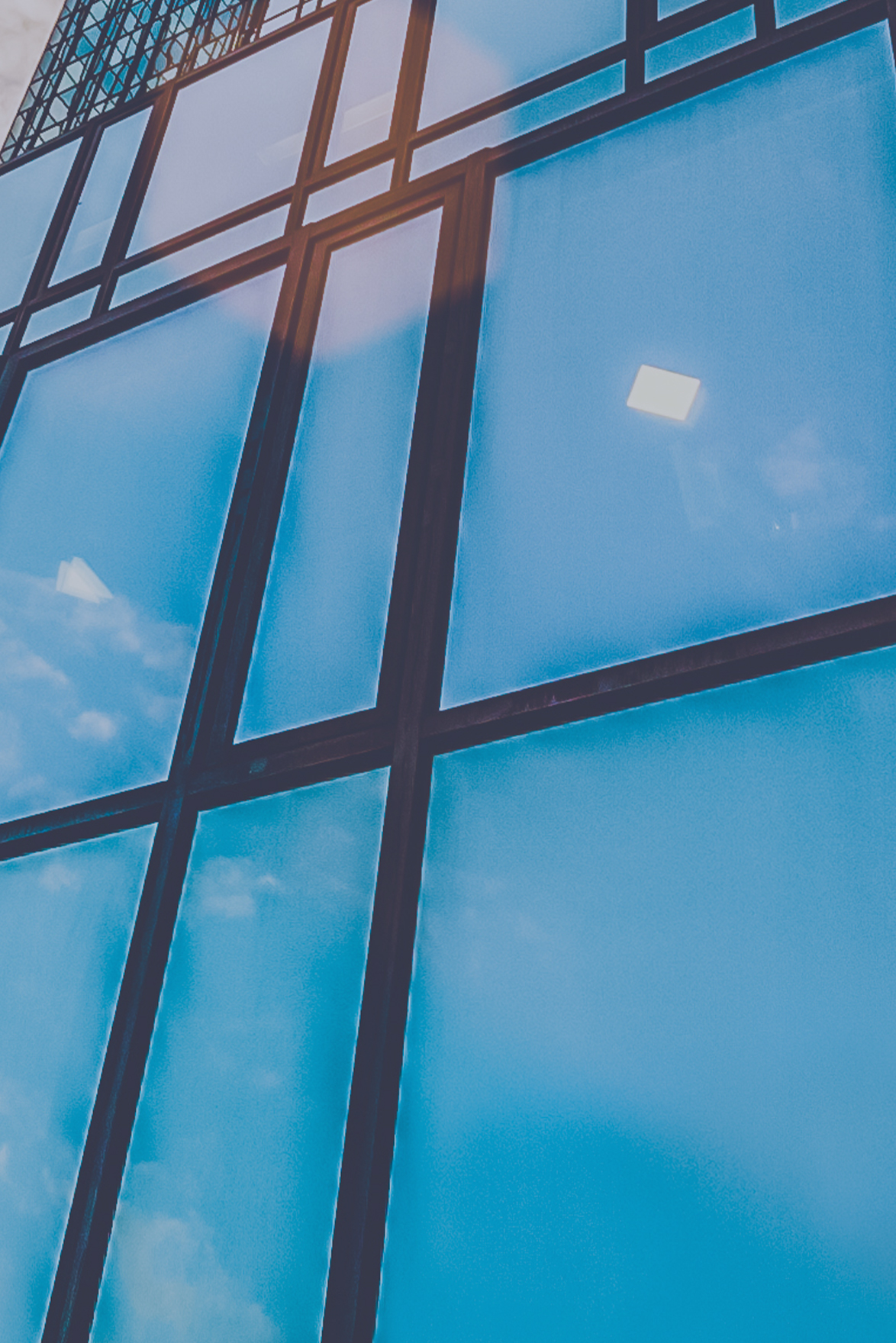 blue sky reflected in side of glass high rise building with different shaped panels with black iron separating them.