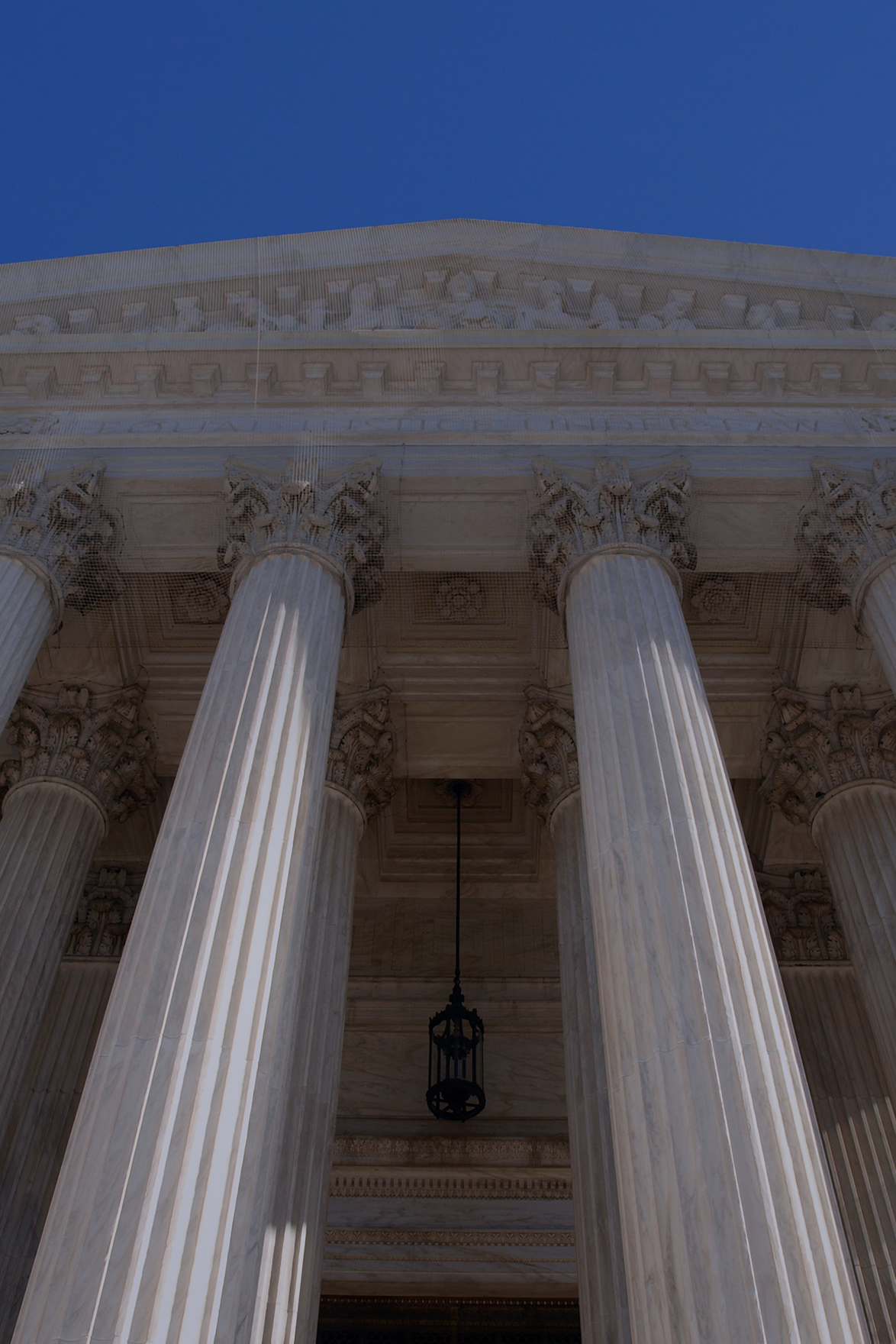 close up looking up from ground level at two white marble columns on a white marble building with blue sky above