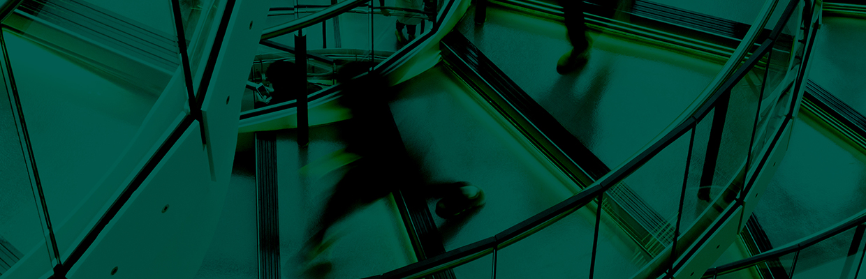 a teal green overlay of a blurred person (moving) down a glass walled spiral staircase in an office building