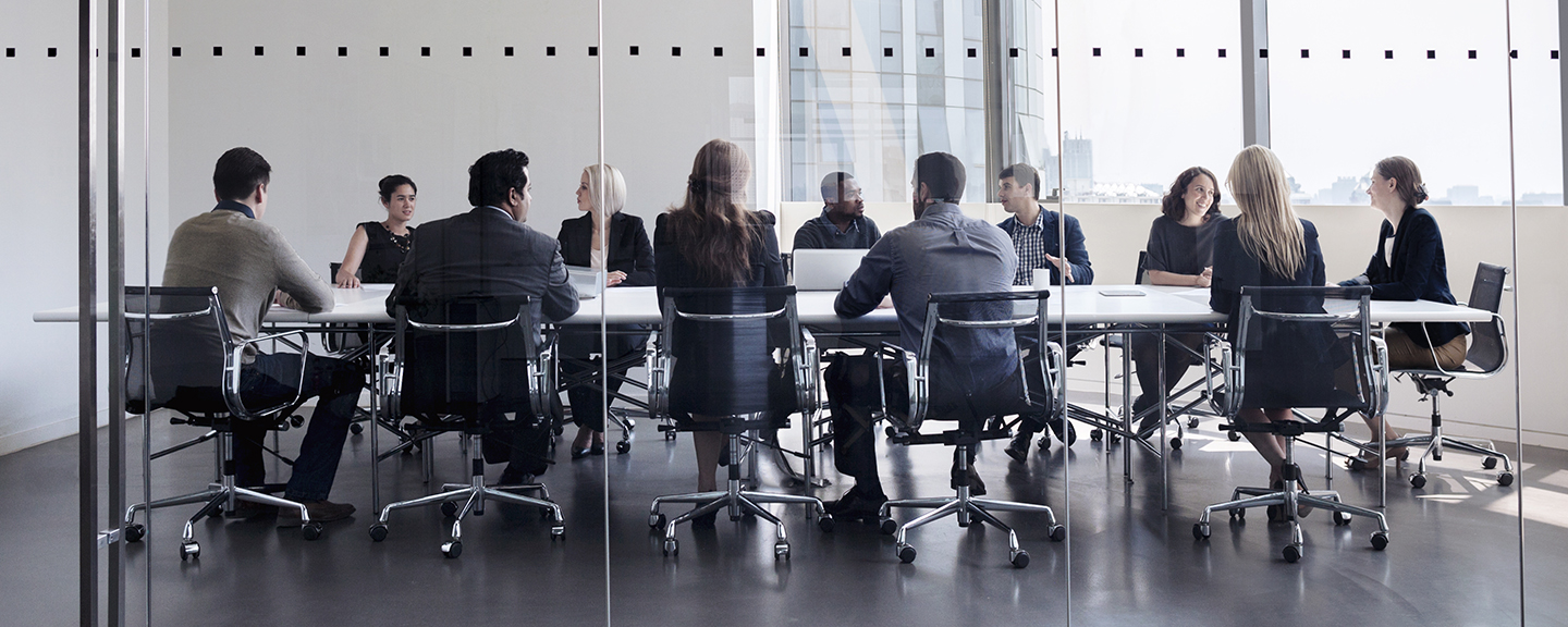business professionals sitting around a large conference room table inside a glass walled room 