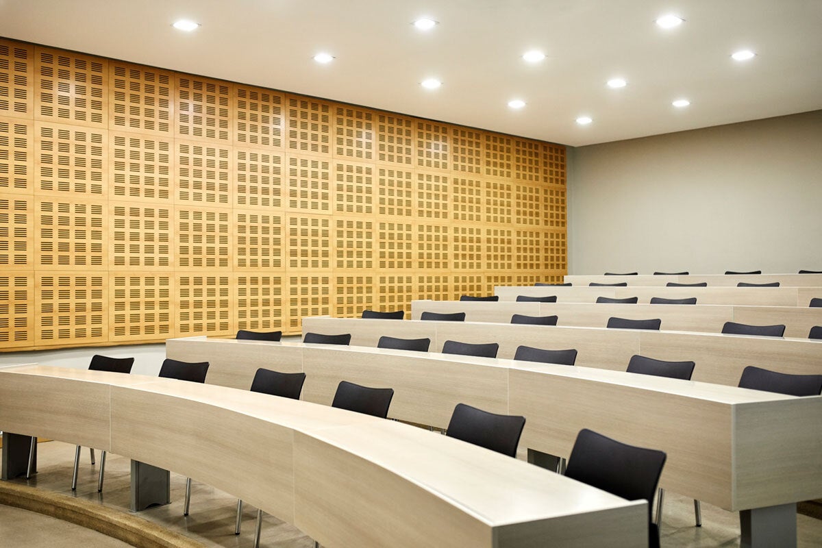 Interior of illuminated lecture hall. Empty chairs are arranged in raised tier classroom. Auditorium in university/school.