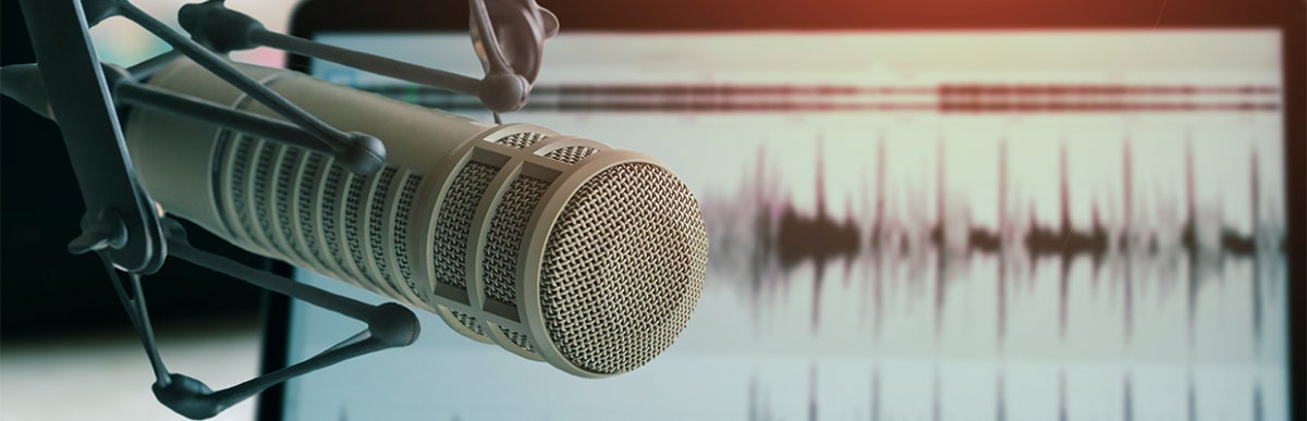 audio microphone close up with a computer screen with an image of an audio file in the background