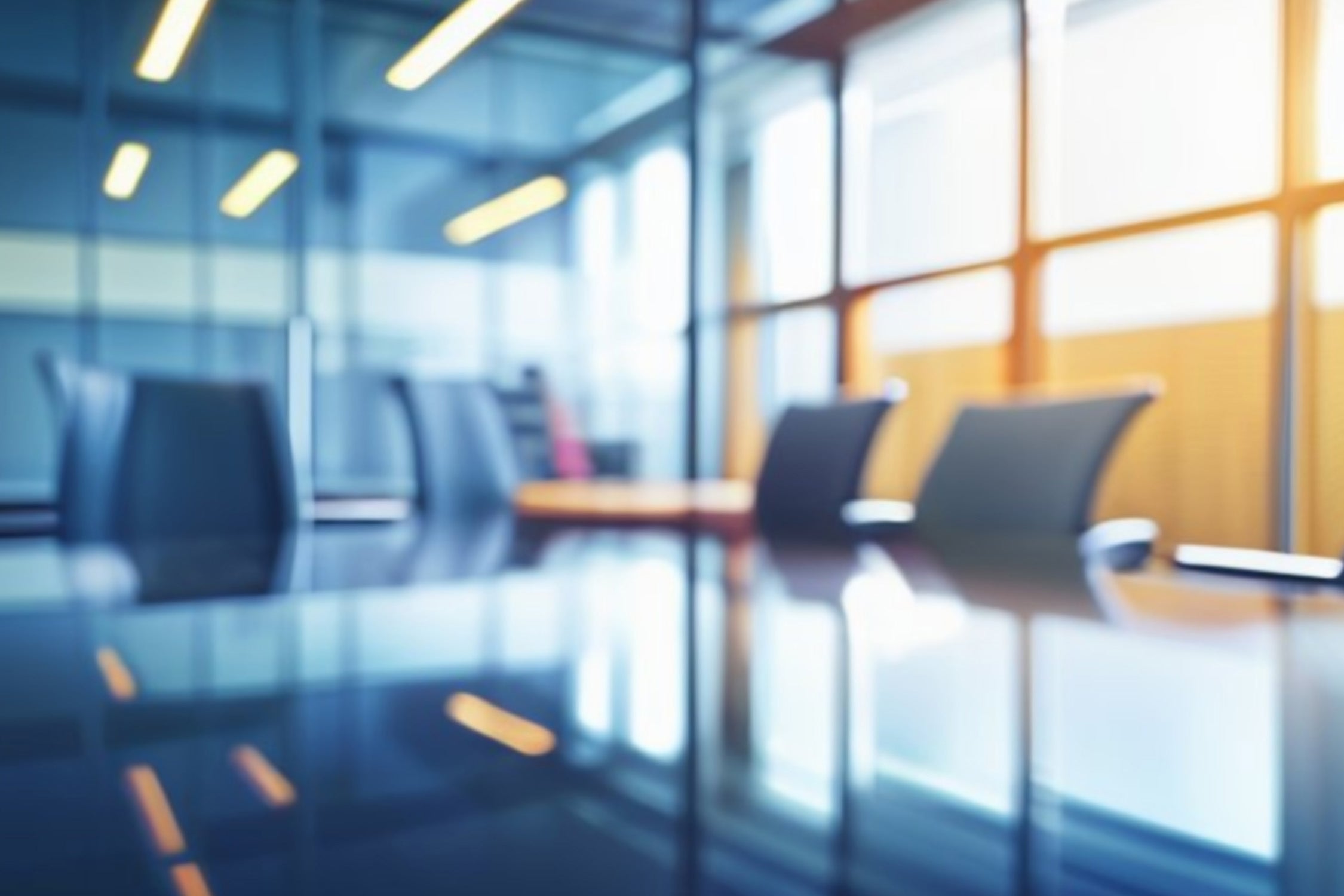 Blurred view of a modern law firm conference room with sleek black chairs around a reflective table, large glass windows, and bright overhead lighting