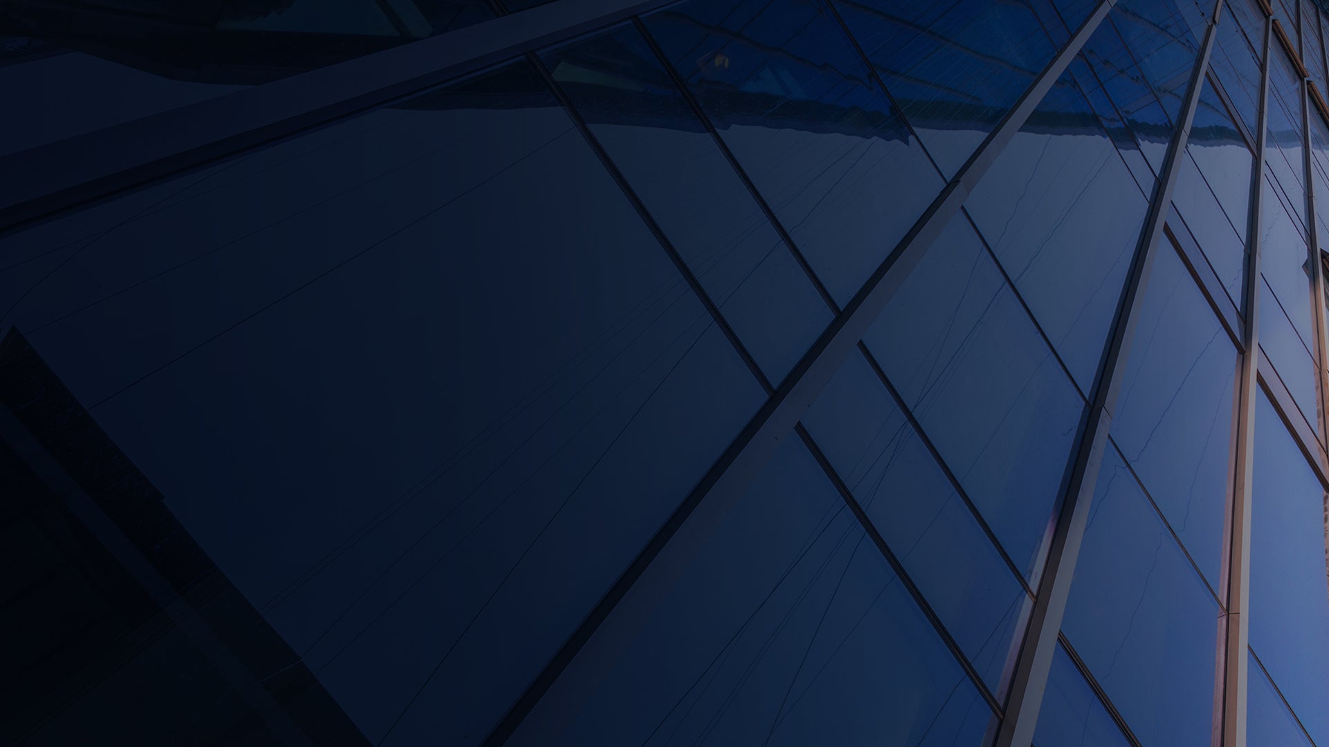 a close-up view of a modern glass building facade. The building's surface is composed of large, reflective glass panels arranged in a grid pattern, with metal frames separating each panel.