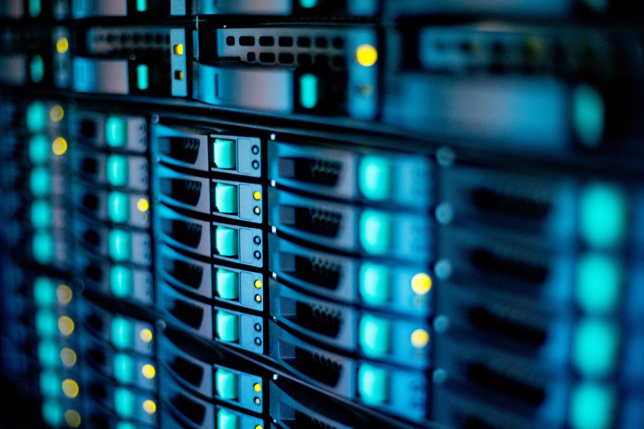Close-up view of illuminated server racks in a dark data center, showing multiple rows of stacked units with glowing blue panels and yellow status lights, conveying secure, high‑performance digital infrastructure suitable for managing sensitive data.