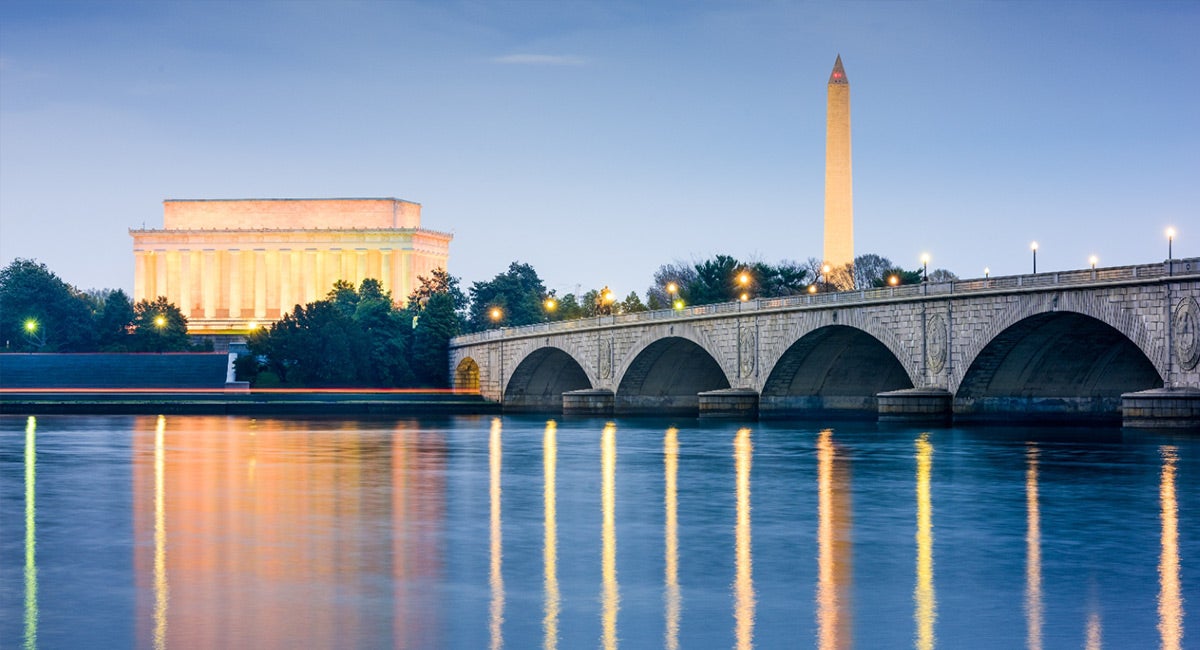 jefferson and Washington monuments with stone bridge over a river at dusk with lights on