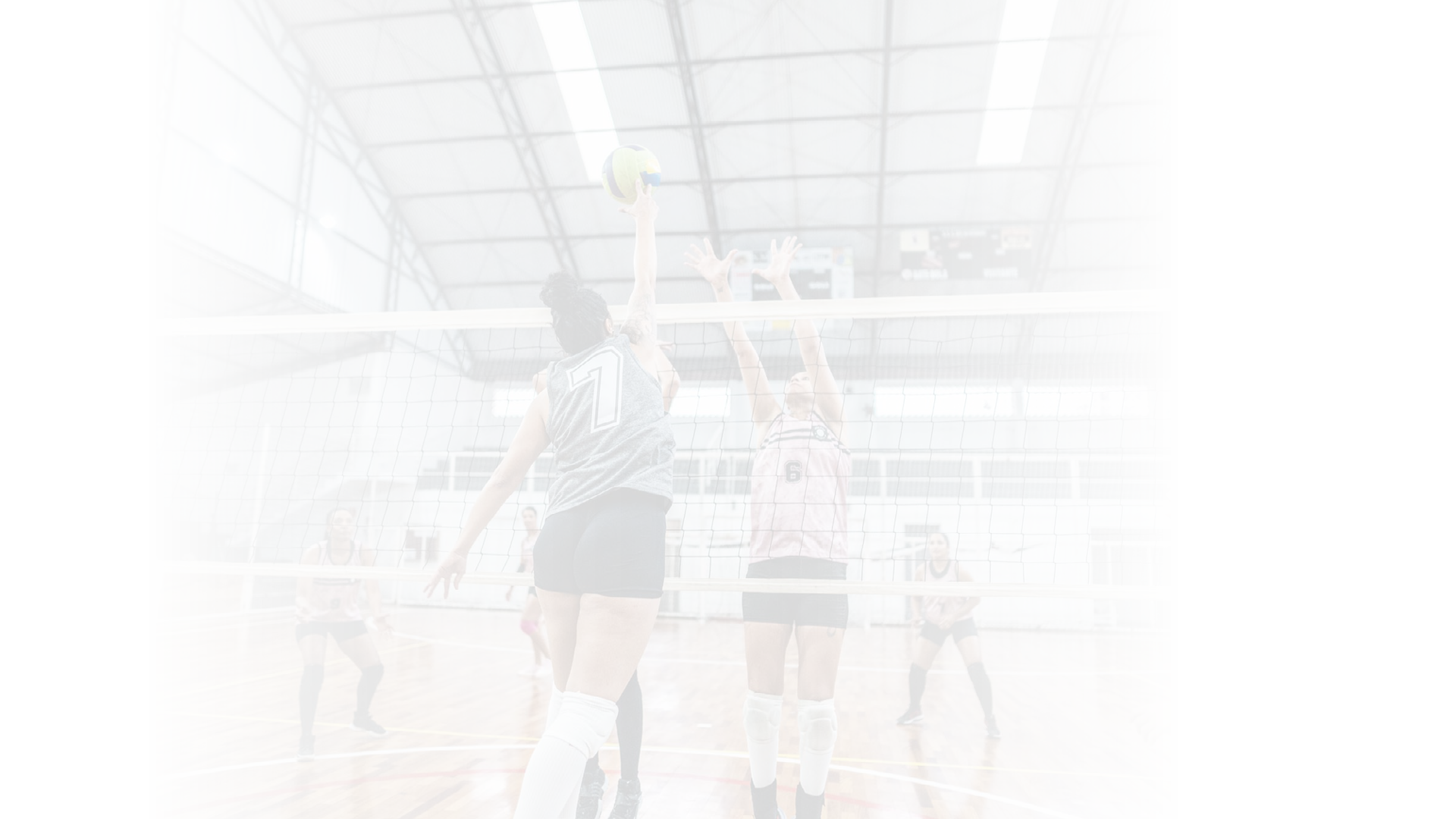 Female volleyball player spiking the ball while other team defending at sports court