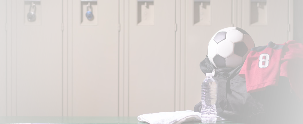 Various sports equipment on bench inside high school or college gymnasium locker room.  Items include: basketball, jersey, water, towel, gym bag..