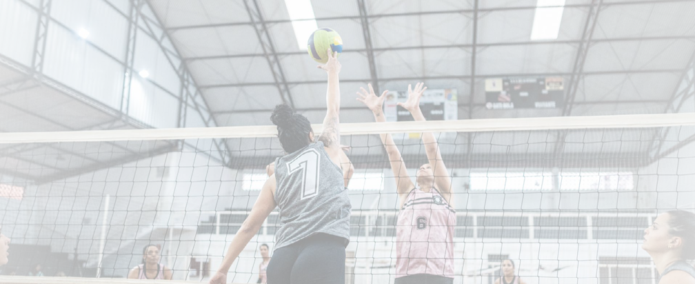 Female volleyball player spiking the ball while other team defending at sports court