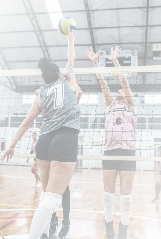Female volleyball player spiking the ball while other team defending at sports court